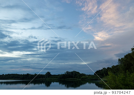 a beautiful blue lake with green tree in the foreground under a dramatic blue dusk sky 93704247