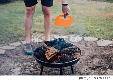 How to Use a Charcoal Grill. Man with Plastic BBQ Hand Fan near Charcoal Grill Fire. Barbeque Plastic BBQ Hand Fan How to Use a Charcoal Grill. Man with Plastic BBQ Hand Fan near Charcoal Grill Fire. Barbeque Plastic BBQ Hand Fan 93704447