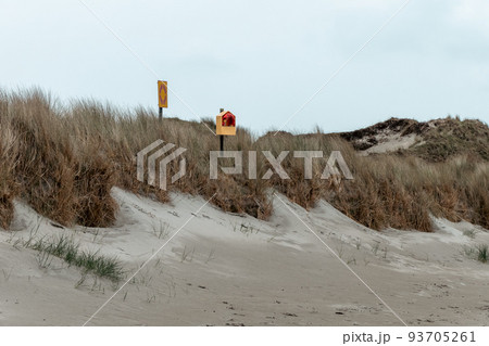 An orange lifebuoy and a sign on the shore under a cloudy sky. Dry grass. Seaside landscape. 93705261