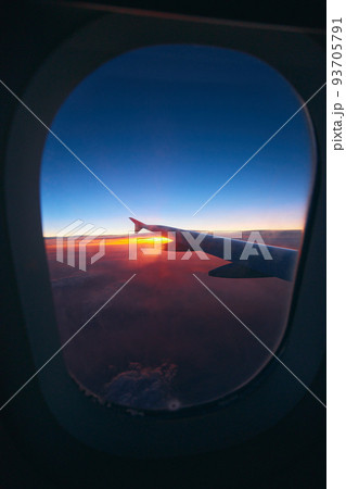 Beautiful sunrise view through the porthole during the flight. Plane wing above the cloudy colorful sunset  93705791