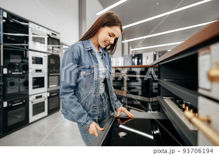 Young brunette woman choosing new electric stove in a hypermarket 93706194