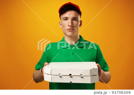 Happy young delivery man holding pizza box against yellow background Happy young delivery man holding pizza box against yellow background 93706309
