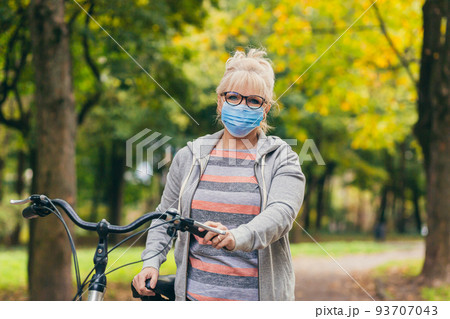 Senior beautiful blonde woman rides a bike in the park, in the woods, in nature in a medical mask during quarantine, leads a healthy active lifestyle Senior beautiful blonde woman rides a bike in the park, in the woods, in nature in a medical mask during quarantine, leads a healthy active lifestyle 93707043