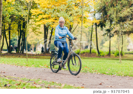 Senior beautiful blonde woman rides a bike in the park, in the woods, in nature, listens to music, spends time actively, plays sports, happy Senior beautiful blonde woman rides a bike in the park, in the woods, in nature, listens to music, spends time actively, plays sports, happy 93707045