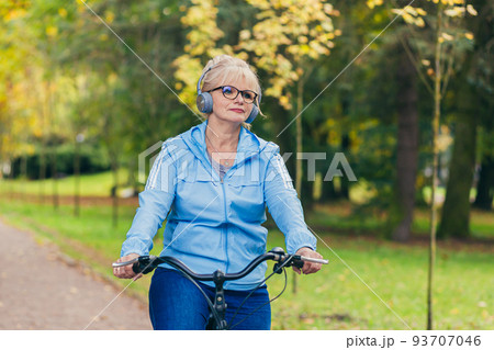 Senior beautiful blonde woman rides a bike in the park, in the woods, in nature, listens to music, spends time actively, plays sports, happy Senior beautiful blonde woman rides a bike in the park, in the woods, in nature, listens to music, spends time actively, plays sports, happy 93707046