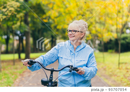 Senior beautiful blonde woman rides a bike in the park, in the woods, in nature, listens to music, spends time actively, plays sports, happy 93707054