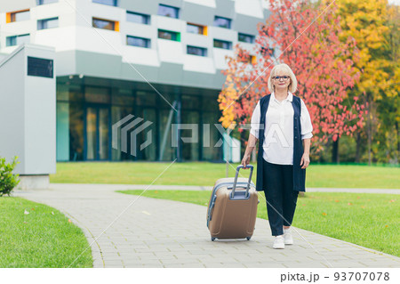 Portrait of a beautiful senior business woman walking with a suitcase near the office center Portrait of a beautiful senior business woman walking with a suitcase near the office center 93707078