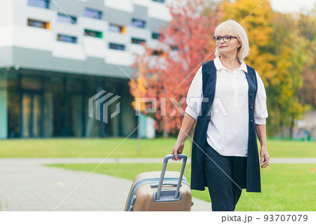 Portrait of a beautiful senior business woman walking with a suitcase near the office center Portrait of a beautiful senior business woman walking with a suitcase near the office center 93707079