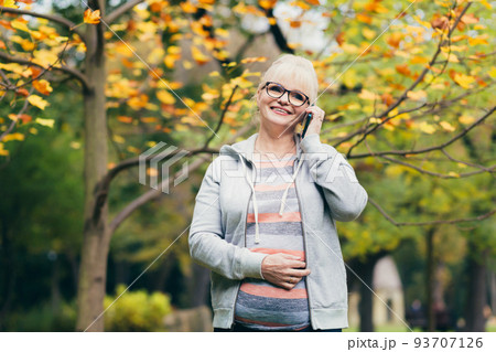Beautiful senior woman in the park on a walk uses the phone, talking on the phone, smiling Beautiful senior woman in the park on a walk uses the phone, talking on the phone, smiling 93707126