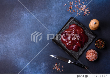 Pieces of raw liver on a wooden cutting board against a dark concrete background 93707452