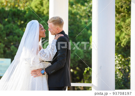 Mixed-racial newlyweds on a walk hugging and lovingly look at each other 93708197