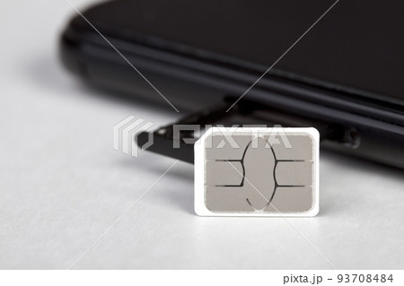 SIM card near the smartphone with an open sim card tray on light background 93708484