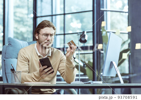 Frustrated and unsatisfied businessman working in modern loft office, freelancer cheated and trying to make bank transaction, using bank credit card and smartphone Frustrated and unsatisfied businessman working in modern loft office, freelancer cheated and trying to make bank transaction, using bank credit card and smartphone 93708591