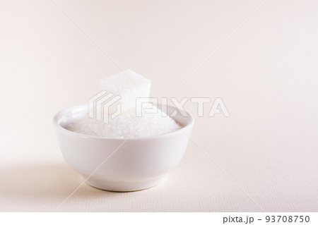 Bowl with granulated sugar and a cube on a pink background. Choosing between types of sugar Bowl with granulated sugar and a cube on a pink background. Choosing between types of sugar 93708750