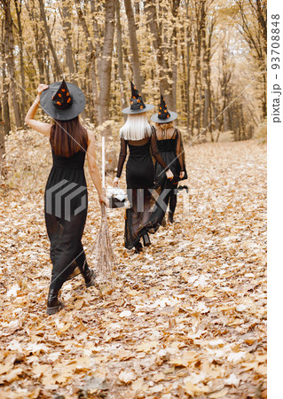 Three girls witches in forest on Halloween. Girls wearing black dresses and cone hats. Witches holding a magician stuff. Three girls witches in forest on Halloween. Girls wearing black dresses and cone hats. Witches holding a magician stuff. 93708848
