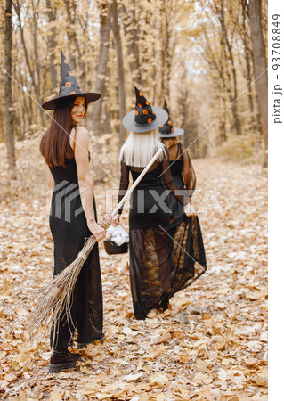 Three girls witches in forest on Halloween. Girls wearing black dresses and cone hats. Witches holding a magician stuff. 93708849