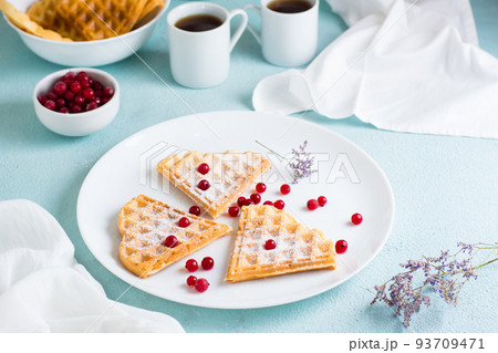 Heart shaped Belgian waffles with red berries and powdered sugar on a plate and two cups of coffee on the table. Valentine's Day 93709471