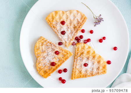 Heart shaped Belgian waffles with red berries and powdered sugar on a plate on the table. Valentine's Day. Top view. Close-up 93709478