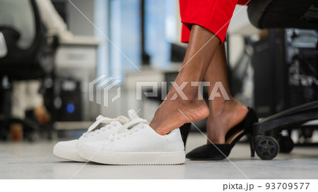 African woman changing from high heels to sneakers in the office. Tired legs. African woman changing from high heels to sneakers in the office. Tired legs. 93709577