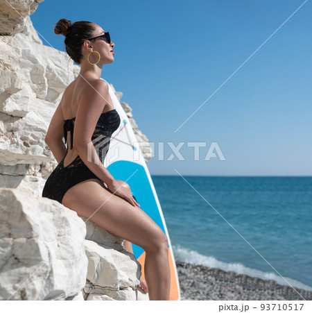 Young teenager girl in swimsuit holding supboard on the beach. AI