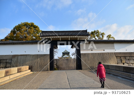日本の大阪府　春の大阪城　入城門から見る美しい天守閣　立派な城壁と綺麗な青空　散歩をする女性 93710625