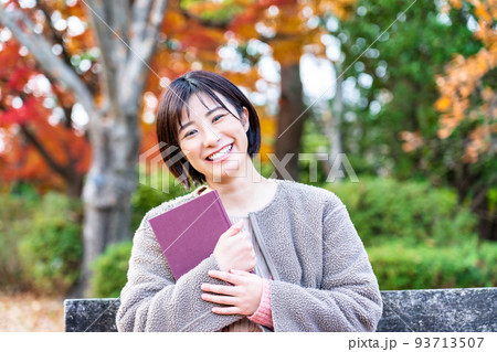 紅葉の公園のベンチで読書をする若い女性 紅葉の公園のベンチで読書をする若い女性 93713507