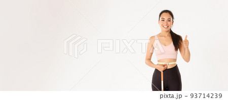 Fitness, healthy lifestyle and wellbeing concept. Portrait of satisfied smiling, cute asian girl in sportswear, showing thumbs-up after measuring waist with tape measure, lost weight Fitness, healthy lifestyle and wellbeing concept. Portrait of satisfied smiling, cute asian girl in sportswear, showing thumbs-up after measuring waist with tape measure, lost weight 93714239