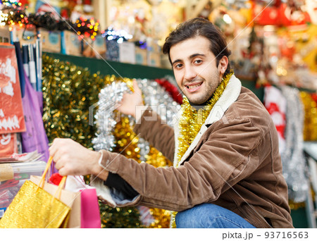 Man with garland choosing decorations at Christmas market Man with garland choosing decorations at Christmas market 93716563