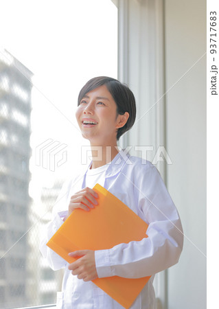 窓際でファイルを抱え微笑む白衣女性_縦3 窓際でファイルを抱え微笑む白衣女性_縦3 93717683