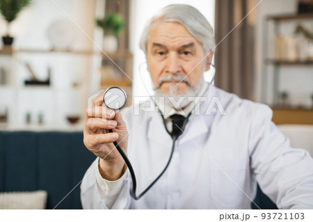 Qualified senior doctor in eyewear and lab coat holding stethoscope while posing at conference room. Qualified senior doctor in eyewear and lab coat holding stethoscope while posing at conference room. 93721103