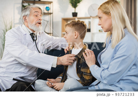 Sick boy sitting on the couch with mother, while male doctor listening his heartbeat Sick boy sitting on the couch with mother, while male doctor listening his heartbeat 93721233