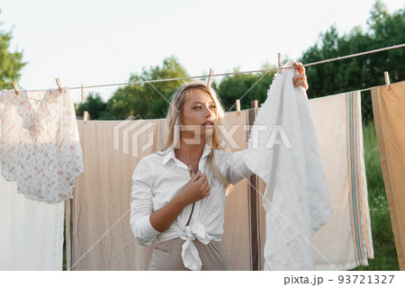 Laundry day. A woman hangs linen and towels on a tree in the courtyard of a village house. Laundry day. A woman hangs linen and towels on a tree in the courtyard of a village house. 93721327
