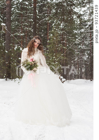 Beautiful bride in a white dress with a bouquet in a snow-covered winter forest. Portrait of the bride in nature Beautiful bride in a white dress with a bouquet in a snow-covered winter forest. Portrait of the bride in nature 93721439