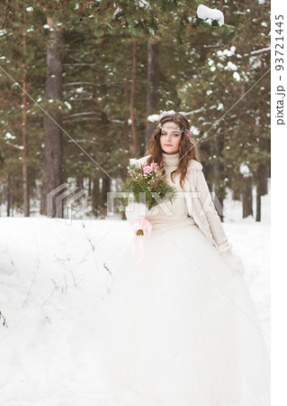 Beautiful bride in a white dress with a bouquet in a snow-covered winter forest. Portrait of the bride in nature Beautiful bride in a white dress with a bouquet in a snow-covered winter forest. Portrait of the bride in nature 93721445