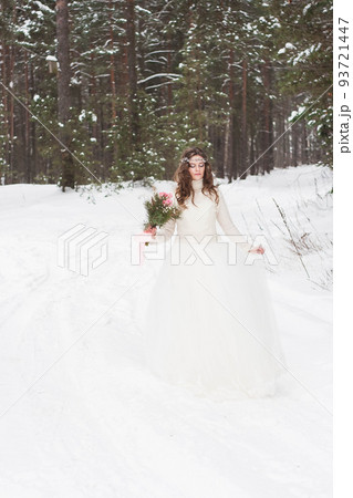 Beautiful bride in a white dress with a bouquet in a snow-covered winter forest. Portrait of the bride in nature 93721447