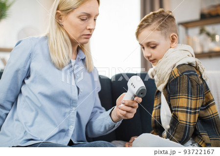 Mother taking care of her cute sick teen boy suffering from cold, checking temperature Mother taking care of her cute sick teen boy suffering from cold, checking temperature 93722167