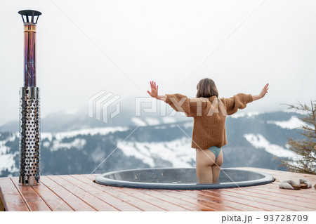 Woman going to rest in hot tub on terrace with great view on snowy mountains 93728709