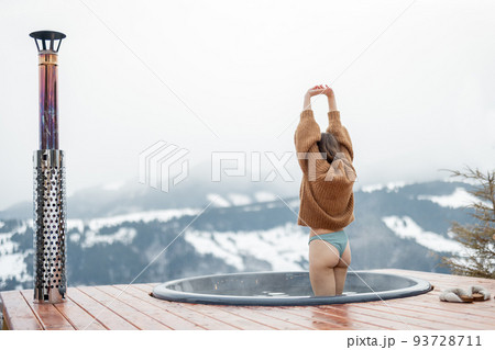 Woman going to rest in hot tub on terrace with great view on snowy mountains 93728711