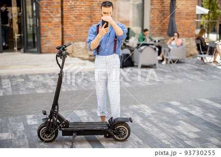 Stylish guy use phone while standing near his electric scooter outdoors Stylish guy use phone while standing near his electric scooter outdoors 93730255