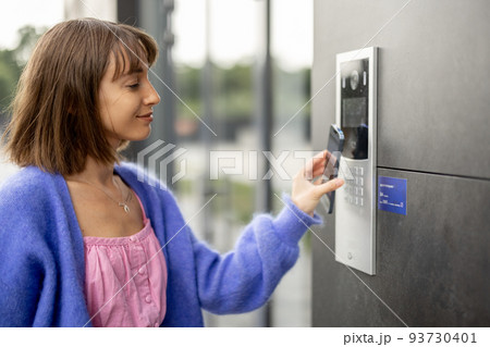 Young stylish woman getting access to the building by attaching smartphone to intercom Young stylish woman getting access to the building by attaching smartphone to intercom 93730401