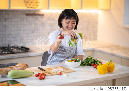 A young asian woman in the kitchen cooking and looking contented 93733157