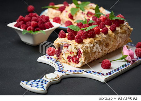 Baked meringue roll with cream and fresh red raspberry on a black wooden board Baked meringue roll with cream and fresh red raspberry on a black wooden board 93734092