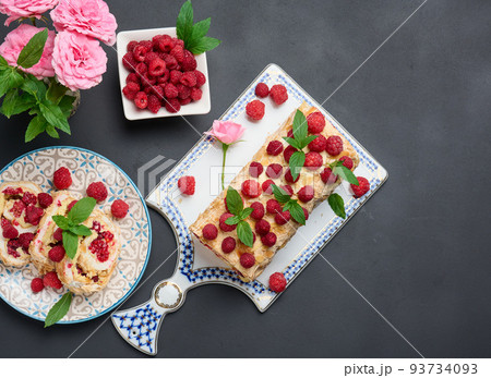 Baked meringue roll with cream and fresh red raspberry on a black wooden board 93734093