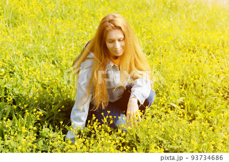 Woman on a yellow ranunculus meadow. A woman sits in a field among yellow buttercups. Portrait of a woman in buttercups 93734686