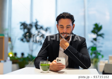 Portrait of happy handsome Hispanic businessman at coffee shop having green tea and using phone Portrait of happy handsome Hispanic businessman at coffee shop having green tea and using phone 93735102