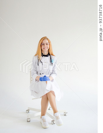 a doctor girl with red hair is sitting on a chair on a white isolated background. a doctor girl with red hair is sitting on a chair on a white isolated background. 93738716