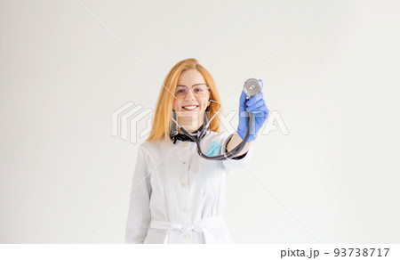 a doctor girl with red hair holds a stethoscope in her hands on a white isolated background. 93738717