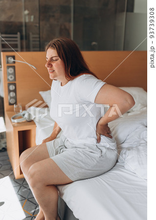 Female sitting on bed in the morning and touching back. Sickness concept, muscular pain. Young beautiful woman has back pain on bed at home Female sitting on bed in the morning and touching back. Sickness concept, muscular pain. Young beautiful woman has back pain on bed at home 93739308