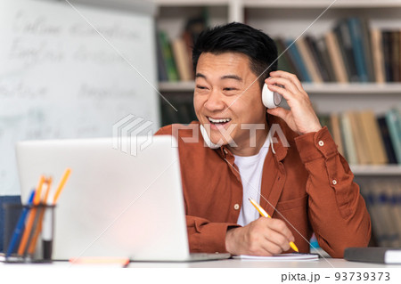 Korean Male Teacher Using Laptop Taking Notes Wearing Headphones Indoors Korean Male Teacher Using Laptop Taking Notes Wearing Headphones Indoors 93739373