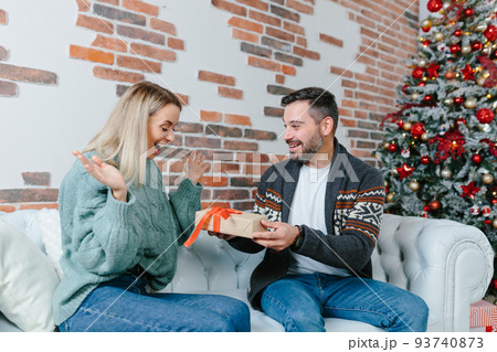 Young family together celebrate New Year and Christmas, couple man and woman give gifts to each other sitting on sofa at home happy and in love 93740873